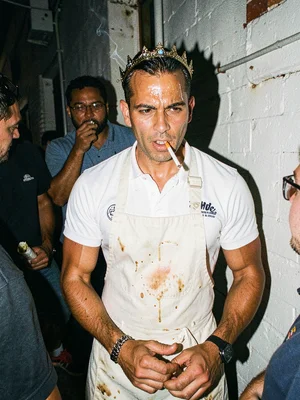 Line cook on break in an alley, apron stained, cigarette lit, flash making the g