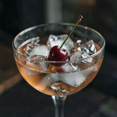 Moody close-up of a cocktail with a luxardo cherry sinking through the ice