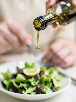 Single drop of olive oil falling from bottle lip, captured sharp mid-air, salad 
