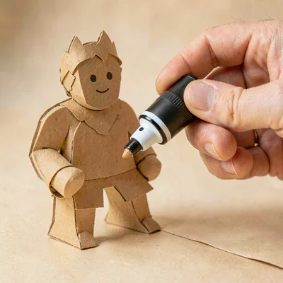 Papercraft hero of a layered paper-cut hand uncapping a paper-cut marker, warm h