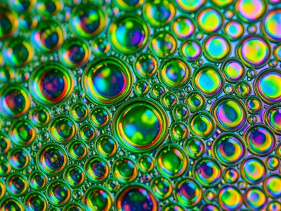 Dense packed oil bubble field on green-lit water, cells touching and deforming i