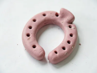 Shod dusty-rose horseshoe with thumb-pressed nail holes and fingernail dents alo