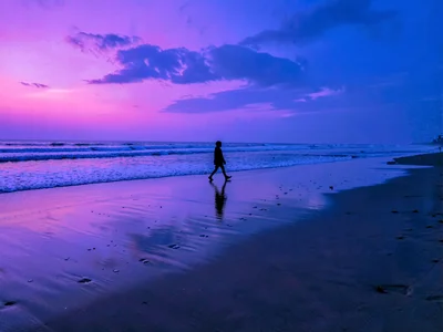 Solitary figure walking tide line at blue hour, wet sand reflecting impossible p
