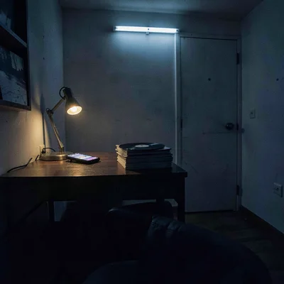 Late-night room interior with a glowing phone on a desk beside a stack of vinyl,