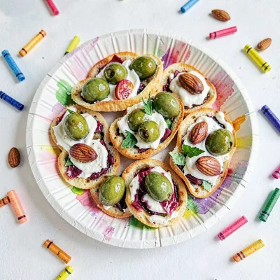 A pop-up paper plate of tapas with torn-paper olives and crayon almonds scattere