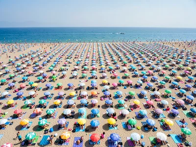 Packed beach from extreme distance, umbrellas and towels forming geometric patte