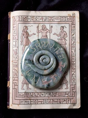 Serpentine jade ornament on dark velvet, studio light picking up carved coil det