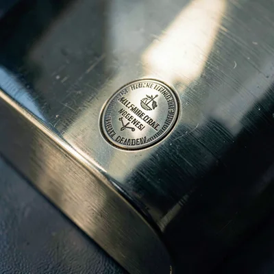 Mineral-cool macro of a polished brass body and engraved badge under cool sideli