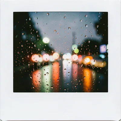 Rain drops on a car windshield, blurred traffic lights beyond creating colored c