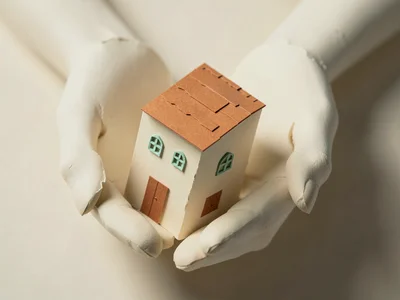 Two oversized paper hands cradle a small folded-cardstock building with terracot