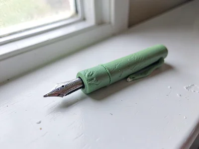 Sketched sage-green fountain pen with a slumped nib and thumb dents along the ba