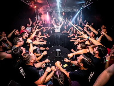 Mosh pit from the center, circle of bodies curving around the frame, fists and s