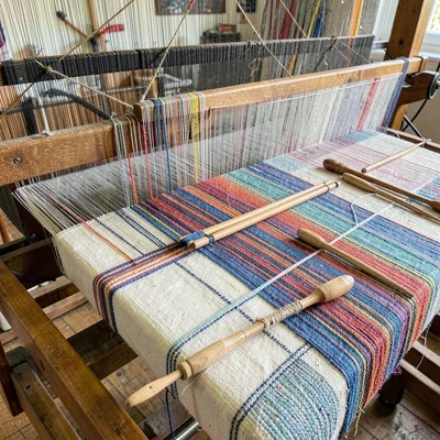 Weaving loom with multiple colored threads creating pattern, shuttles resting on