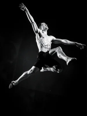A dancer mid-leap, captured at the peak, muscles defined by hard cross-lighting,