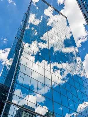 A glass skyscraper reflecting clouds so perfectly it seems to disappear into sky