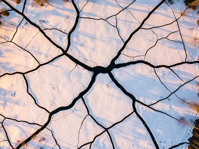 A frozen lake with abstract cracks creating a web pattern, dark water visible in