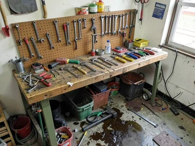 Mechanic's pegboard plus workbench plus oil-stained floor, tools breeding tools,