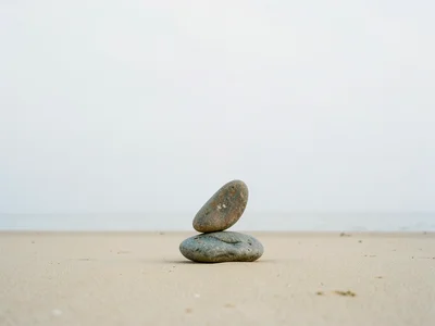 Single stone balanced on another on an empty beach, horizon line dividing frame 