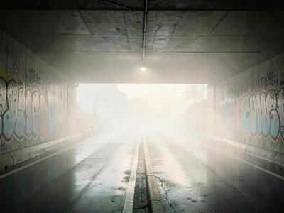 Quiet motorway underpass at first light, graffiti softened by wet air, oncoming