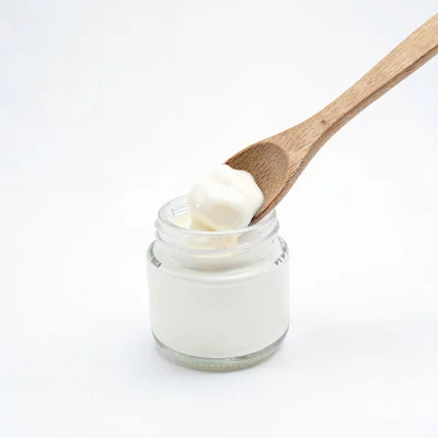 Clean studio macro of a wooden spatula scooping cream from a small jar on white