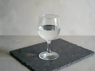 Three-quarter framing of a stemmed glass holding water on chalk paper, soft side