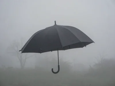 One black umbrella in thick fog, handle barely visible, person implied but never