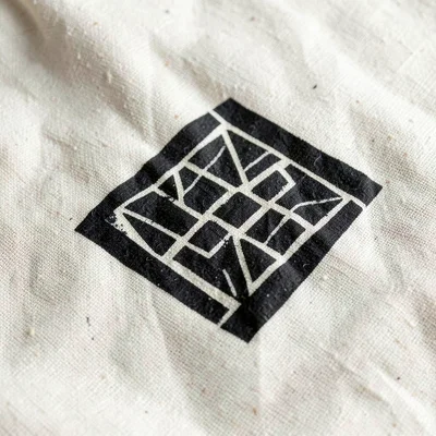 Single Sankofa symbol macro on natural cotton — strong geometric form, black on 