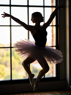 Ballet dancer mid-leap in window light, rim light defining every muscle and tutu