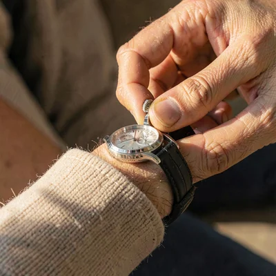 Tight warm closeup of a hand winding the crown of a finished watch, soft cuff fa