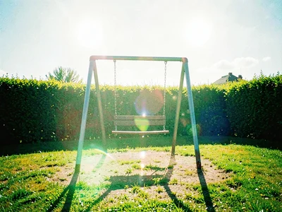 The empty seat of a swing set creaking in midday wind on a vacant playground bor