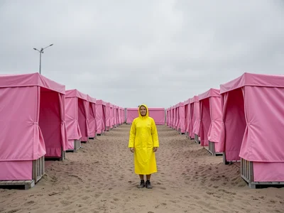 Row of identical pink beach cabanas, centered figure in yellow raincoat, overcas
