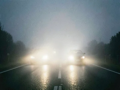 Car headlights cutting through dense fog on empty road, film grain, high contras