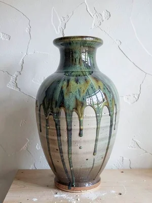 A single large thrown vase with dripping tenmoku glaze against a white plaster w