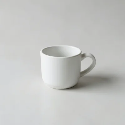 Minimalist studio photograph of a single white coffee cup on a clean matte surface, centered composition, soft diffused 