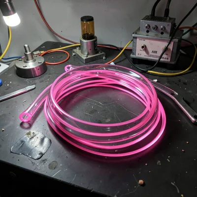 An unlit pink glass tube section coiled loosely on a dark workbench