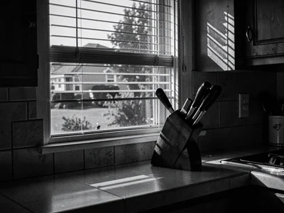 Kitchen window with venetian blind shadows on counter, knife block silhouetted, 