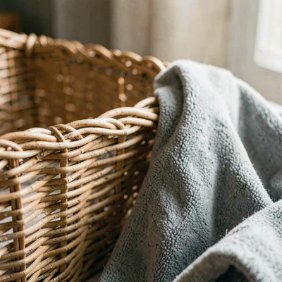 Cropped close-up of a wicker bassinet lining and a soft pebble-grey throw, warm