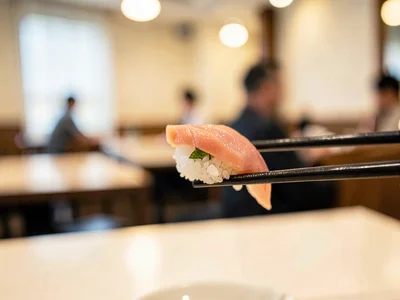 Sushi piece on chopsticks, restaurant behind cream
