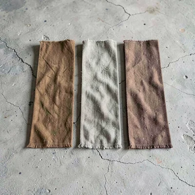 Sculptural lineup of five fabric bolts in muted earth tones on chalky concrete