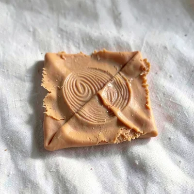 Wiped ochre dish rag folded into a square with thumb-pressed creases, on plain p
