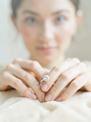 Single diamond engagement ring sharp on velvet, woman's hands and face behind it