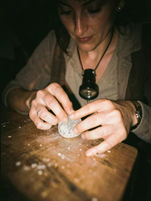 Fingers setting a stone into a bezel, loupe hanging around the neck
