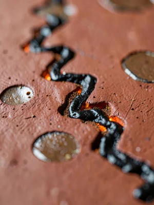 Sgraffito carved zig-zag through black slip on red clay, exposed earth glowing r