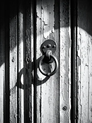 An old wooden door with peeling paint and a heavy iron knocker, deep grain textu
