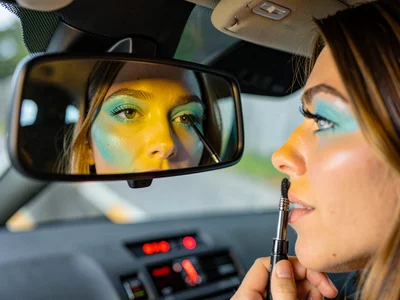 Woman applying mascara in rearview mirror, dashboard light throwing yellow on he