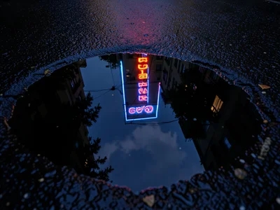Puddle reflecting neon sign, vivid color in dark water surrounded by black wet a