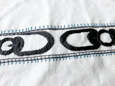 Embroidery border running stitch detail — tiny blue accent stitches beside main 