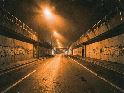 Highway underpass with orange sodium glow, graffiti barely visible in monochrome