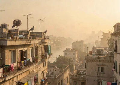 Dusty golden Cairo haze compressing apartment layers, rooftop dovecotes against 