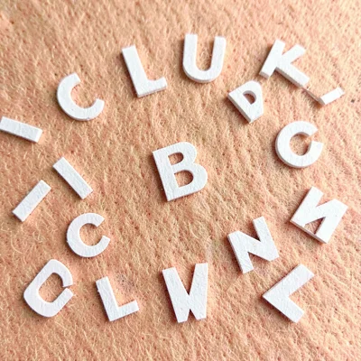 Tiny cardstock alphabet shapes scattered across a peach felt backdrop (abstract 
